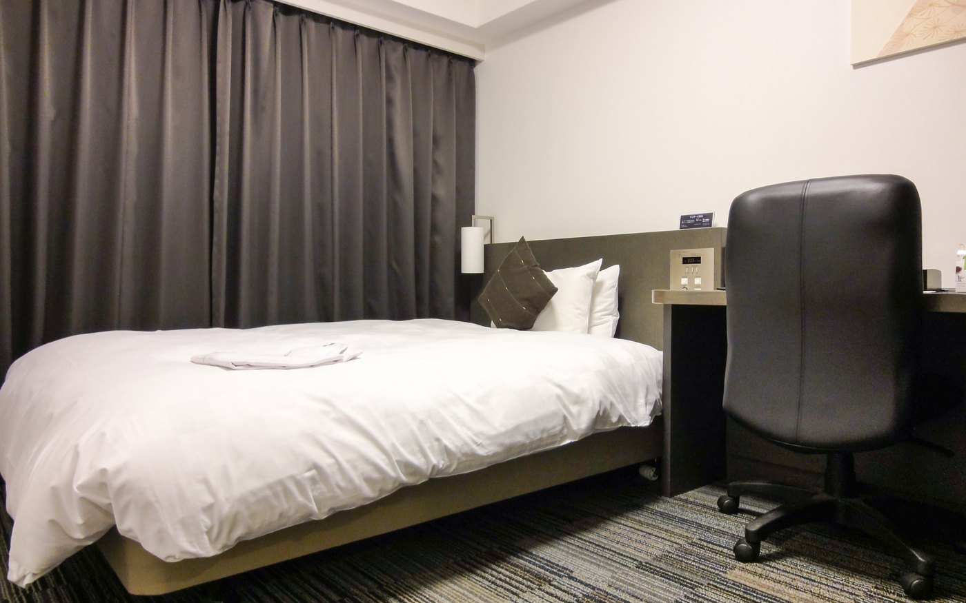 A compact Japanese business hotel room with a double bed, desk and chair