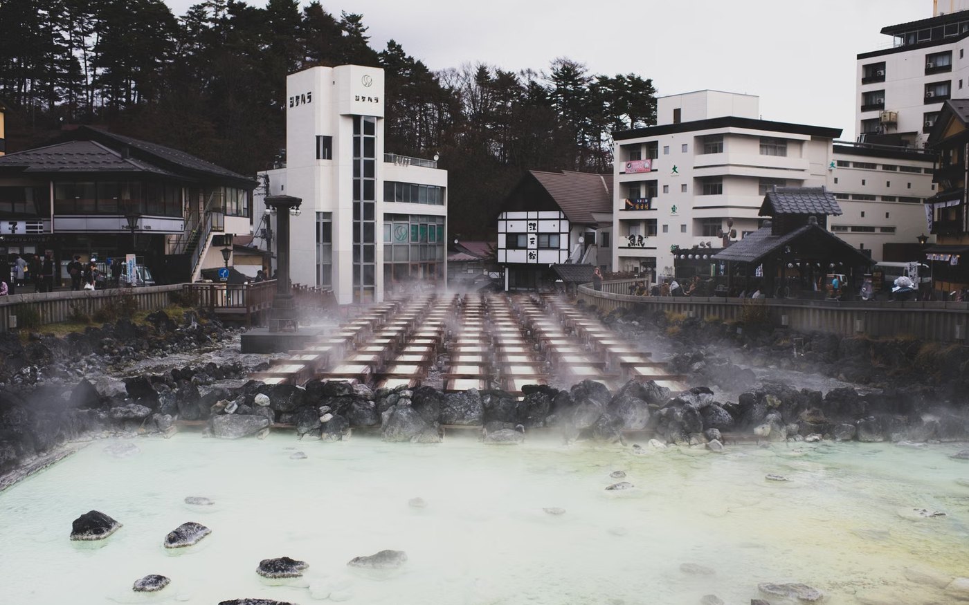 An outdoor hot spring bath with steam rising, set among trees in an onsen town