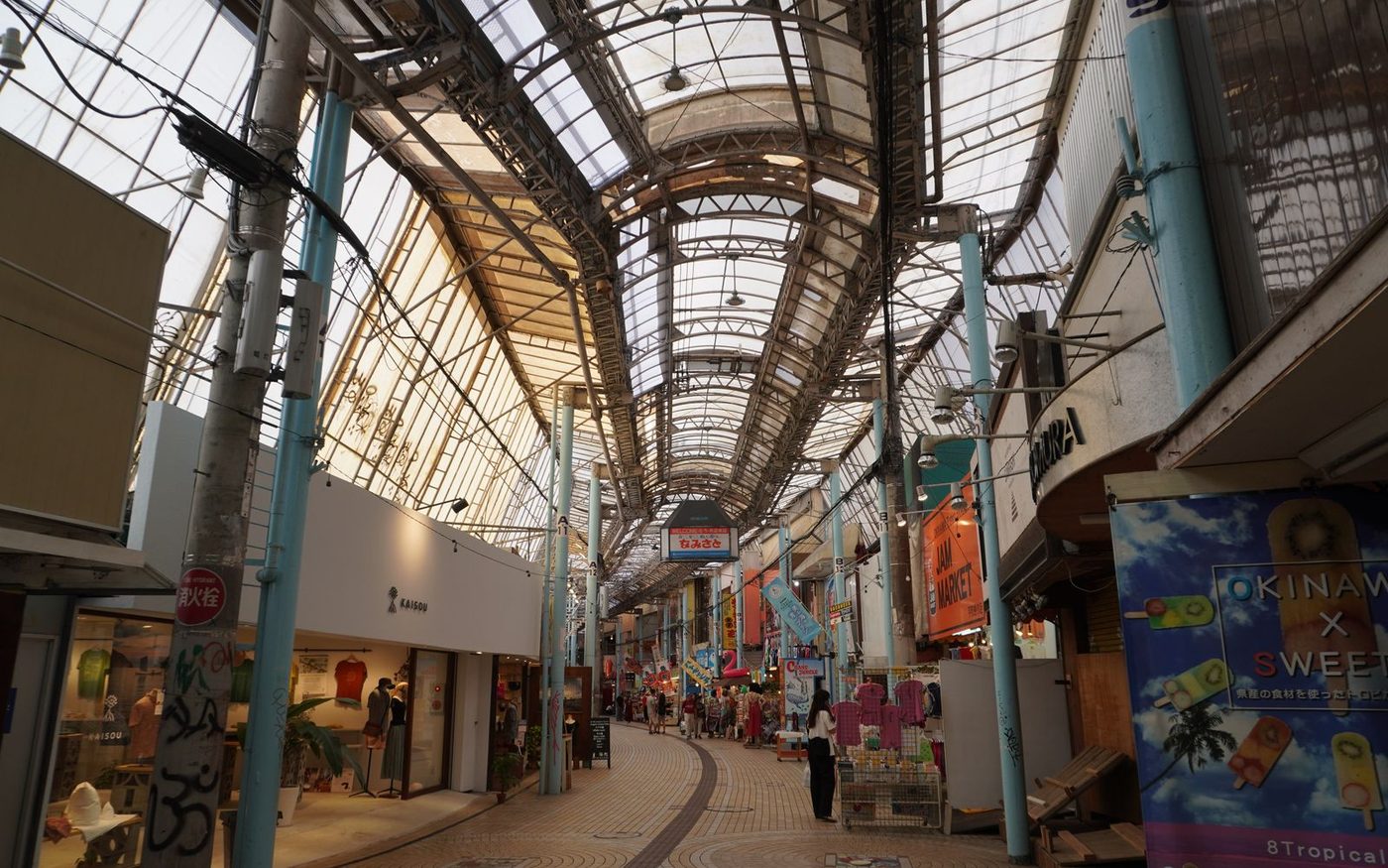 A covered shopping arcade in Naha with a vaulted glass roof and shoppers below