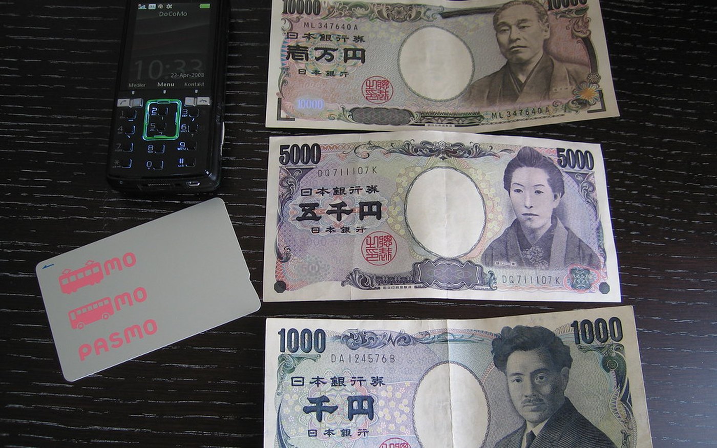 A white PASMO card with pink lettering beside Japanese yen notes on a table