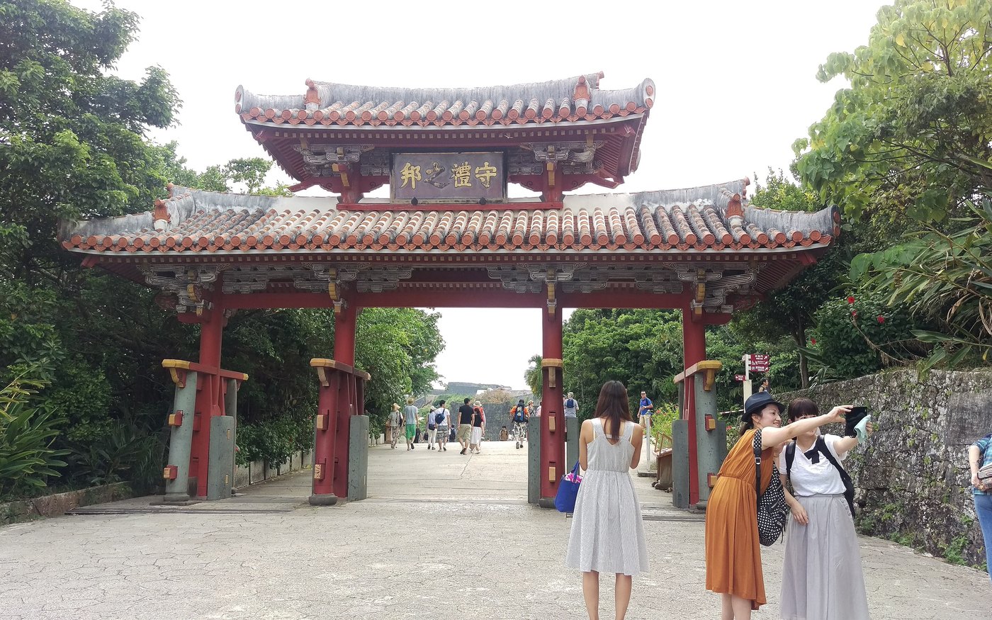 The red two-tier gate of Shureimon at Shuri Castle, its name plaque above the arch and the paved path running through it