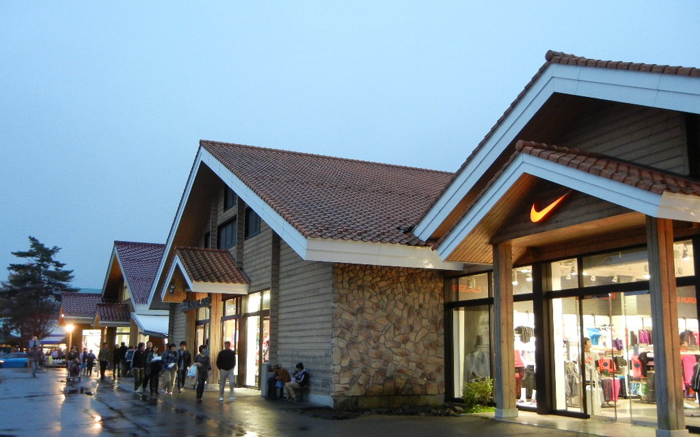 An outdoor outlet village at dusk with shoppers walking past a Nike store