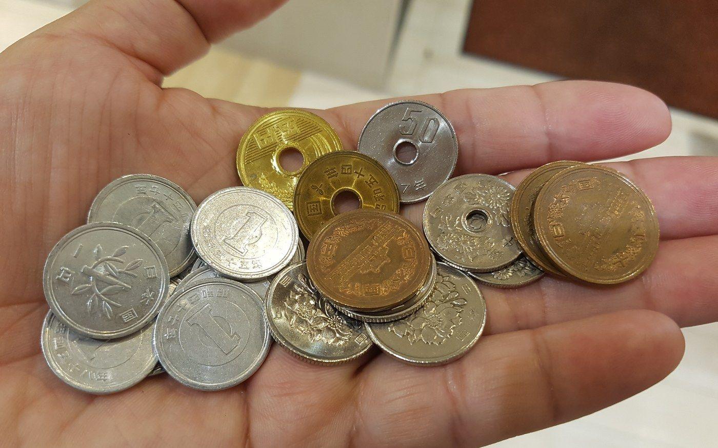 A hand holding a mix of Japanese one, five, ten and fifty yen coins