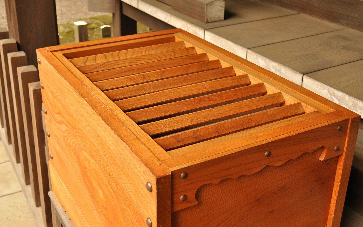 A slatted wooden offering box in front of a shrine, seen from the side