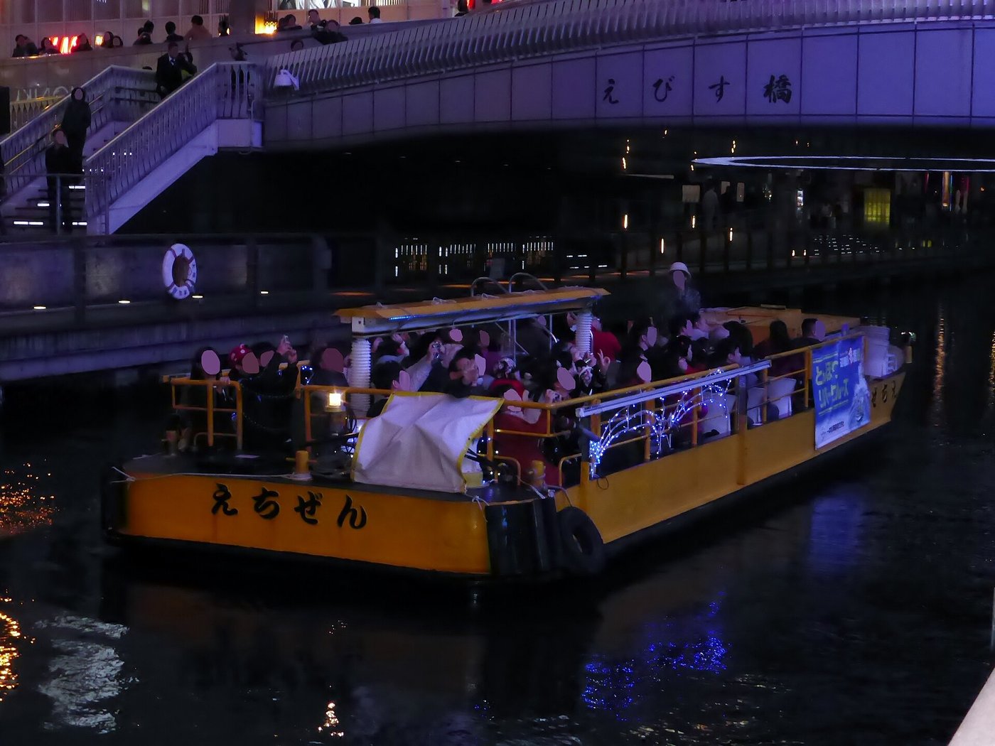 A yellow cruise boat passing under Ebisubashi on the Dotonbori canal at night