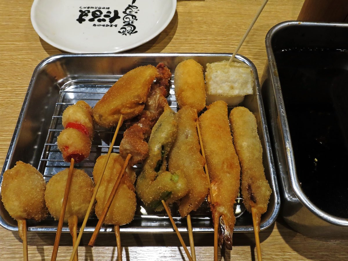 A tray of deep-fried kushikatsu skewers beside a shared container of sauce