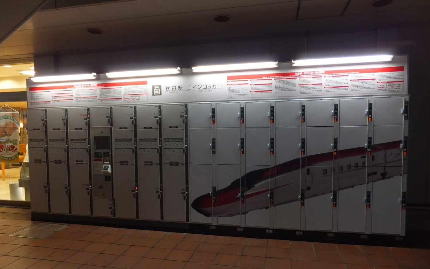 A long bank of coin lockers at a Japanese station, small doors at one end and tall doors at the other