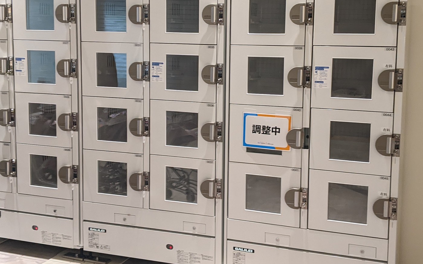 A bank of white lockers with glass doors on a tiled floor