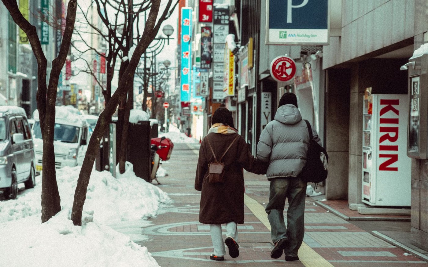 Two people walking on a snow-covered pavement in a Hokkaido city