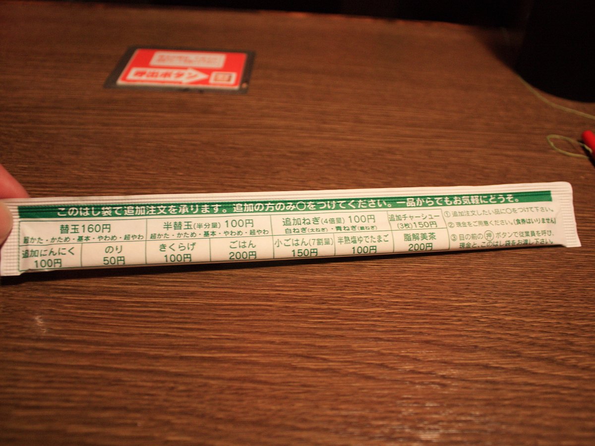 A paper order slip and a small paper bag on a counter at a ramen seat