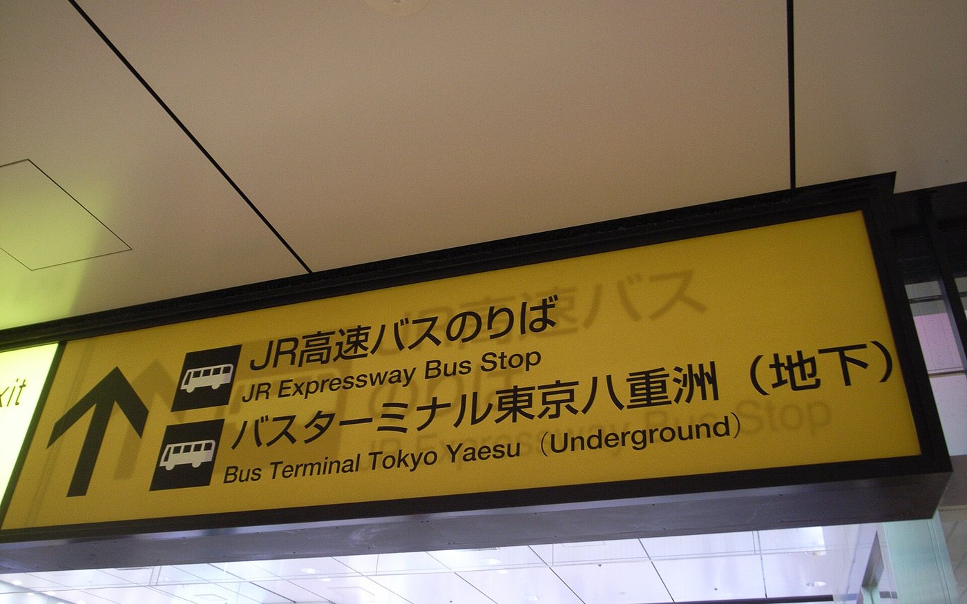 A yellow wayfinding sign inside Tokyo Station pointing to the Yaesu underground highway bus terminal