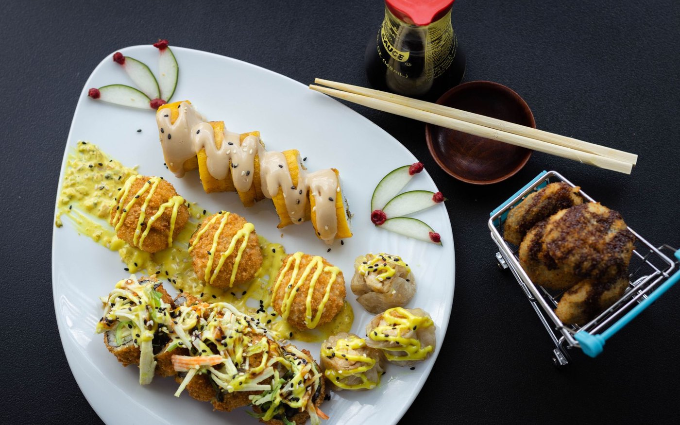 A plate of fried sushi rolls topped with sauces and sesame, with chopsticks and a small condiment bottle