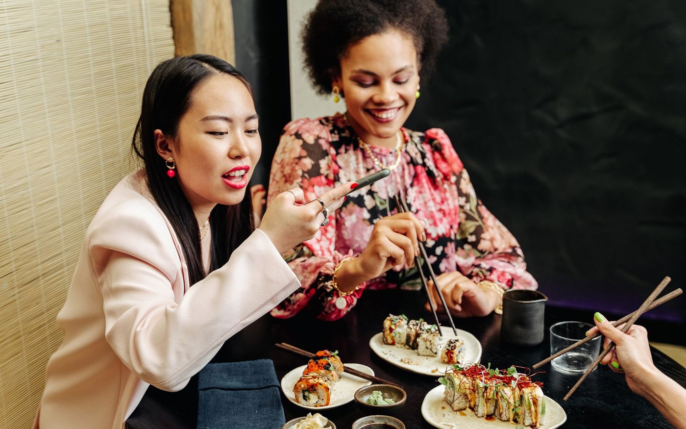 Two people eating sushi rolls at a restaurant table with small plates, chopsticks and a glass