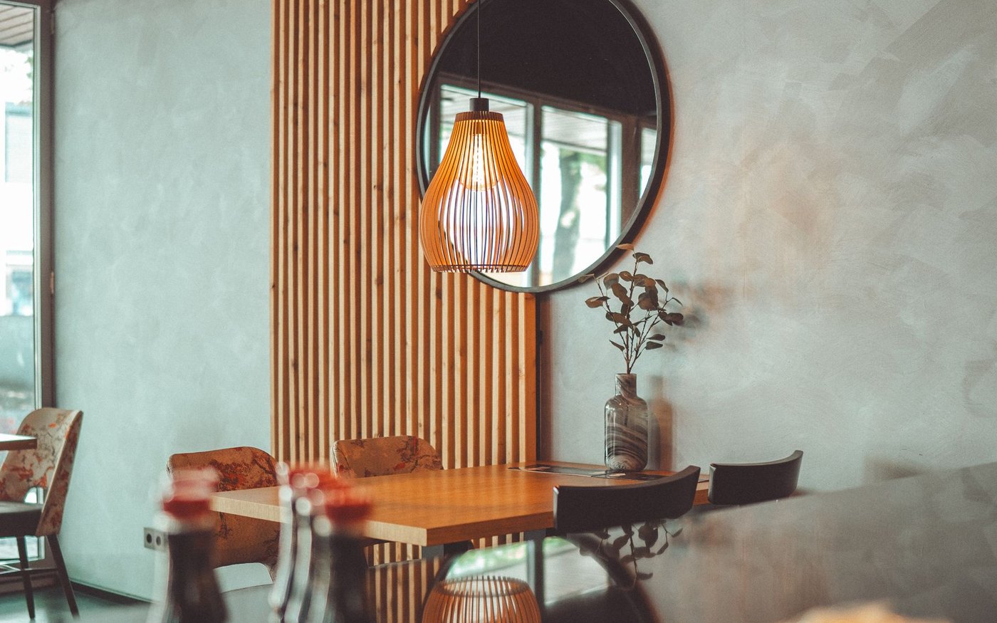 A dining table and chairs in a warmly lit Japanese restaurant, with a wood slat partition and a pendant lamp above