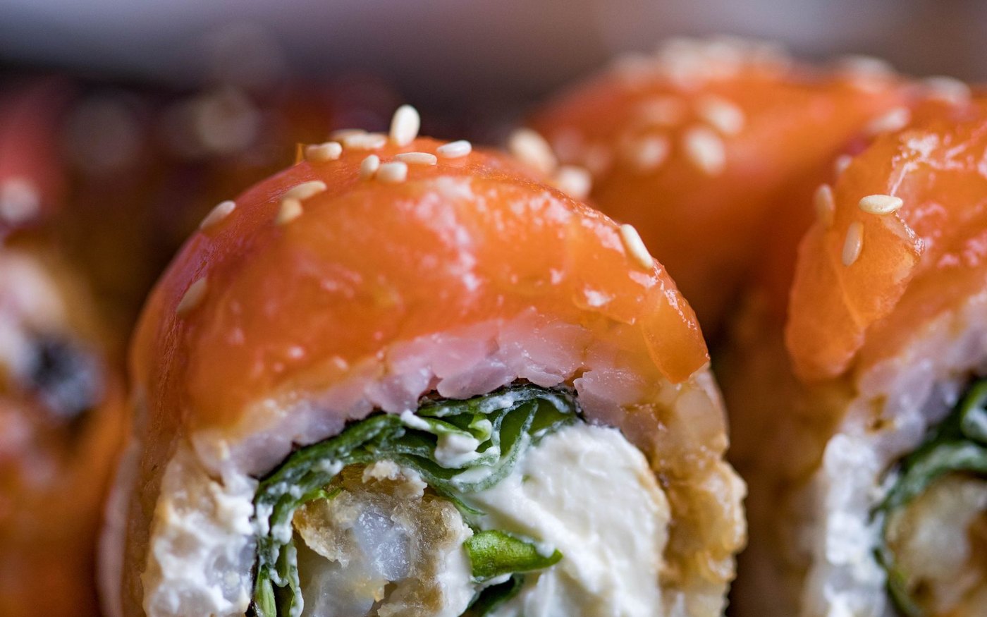 A cut sushi roll topped with salmon and filled with crab and avocado, seaweed around the rice