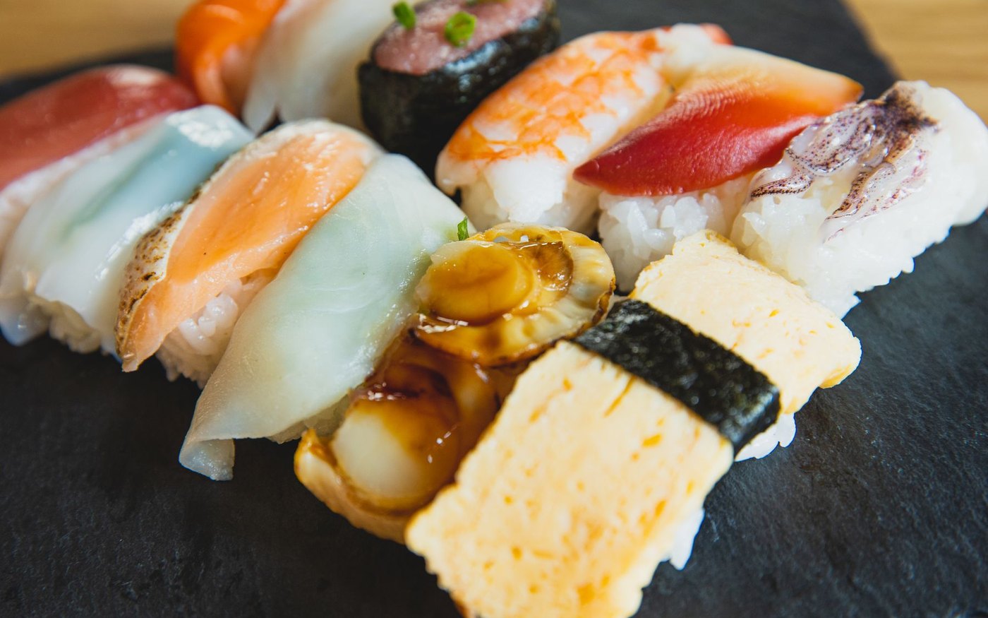 An assortment of nigiri and rolled sushi on a dark slate platter, salmon, prawn, tuna and egg pieces