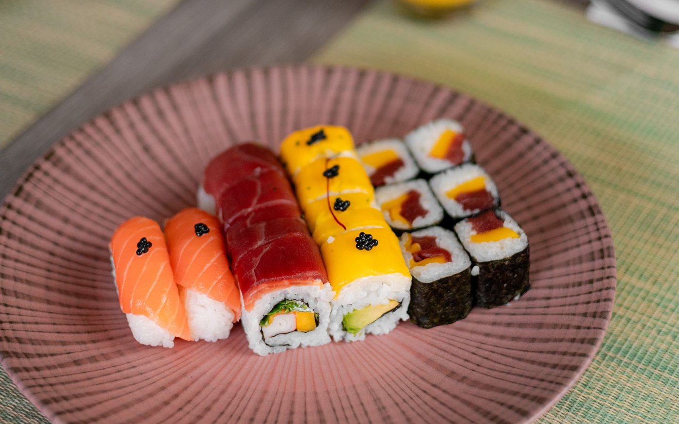 A ribbed plate of mixed sushi, salmon nigiri and cut rolls, on a woven mat