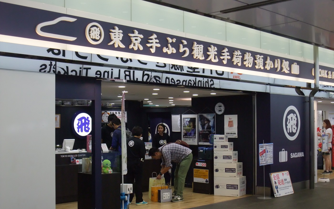 A staffed left-luggage counter inside Tokyo Station with staff behind the desk and stacked boxes