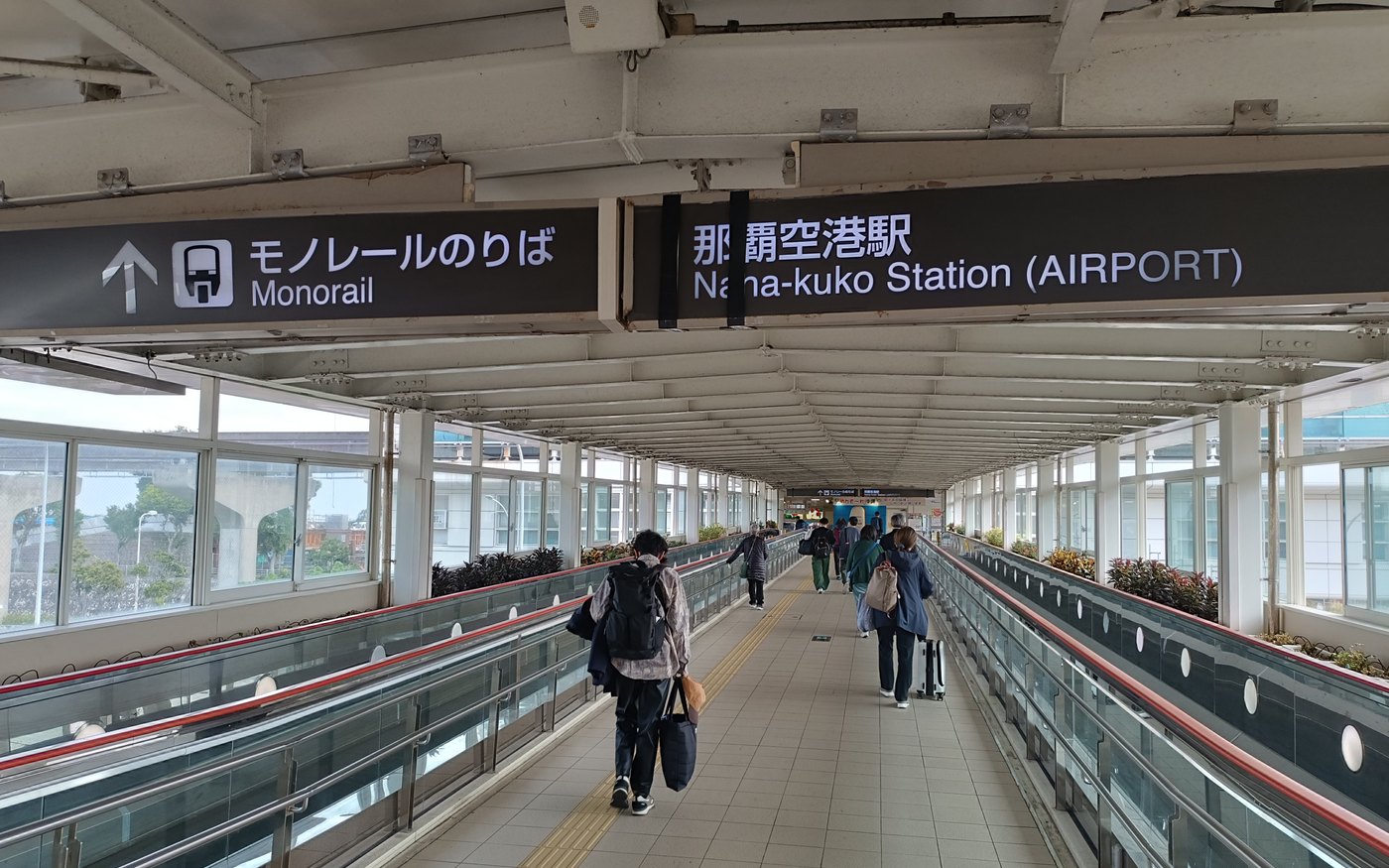 A covered walkway inside Naha Airport with overhead signs directing travellers to the monorail