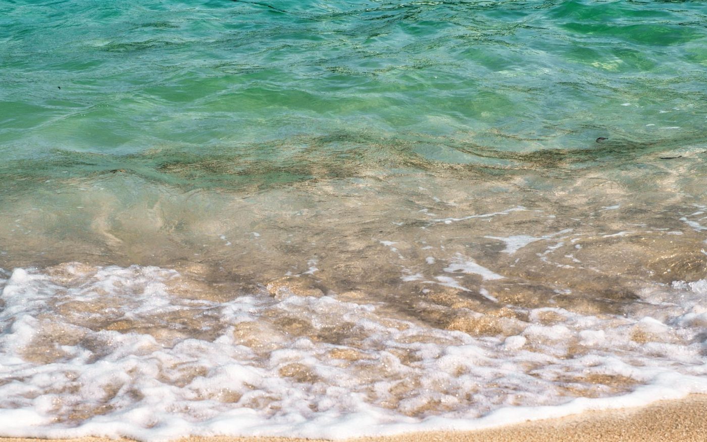 Turquoise water breaking in gentle waves on a pale sandy shore