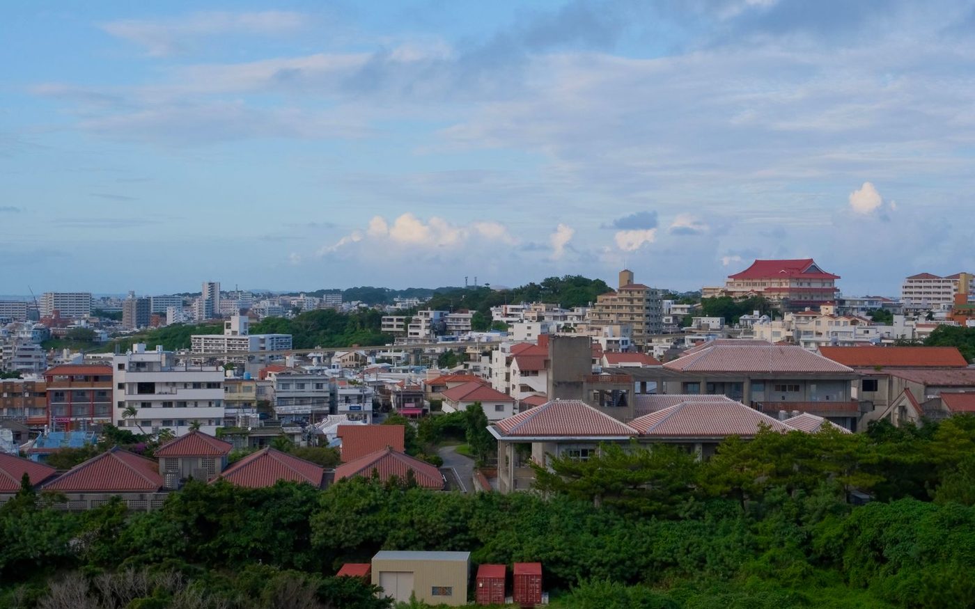 Rooftops and low buildings across Naha seen from above, with trees between them