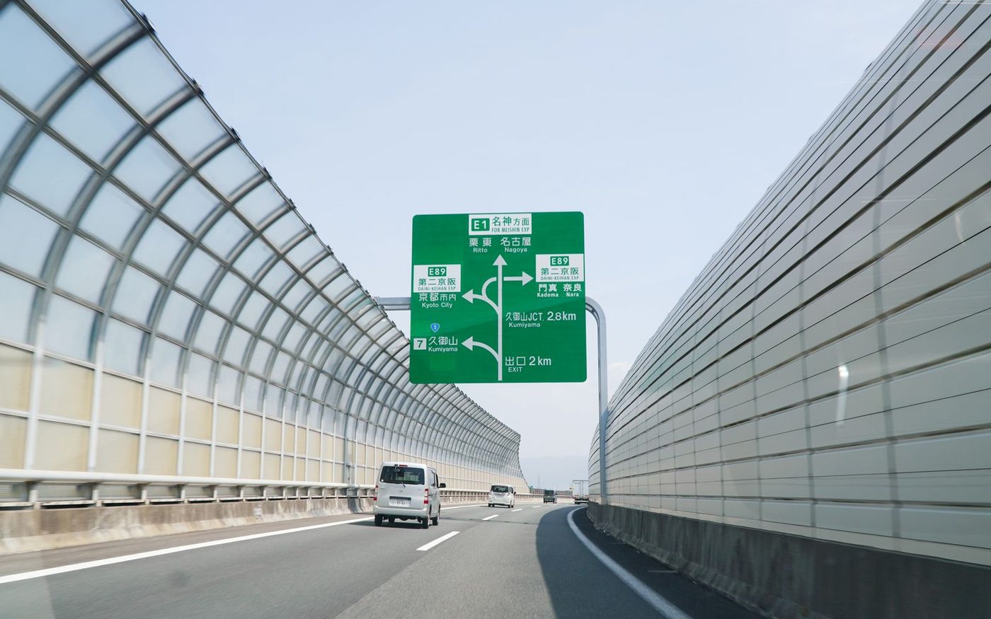 A Japanese expressway with a green overhead direction sign and light traffic