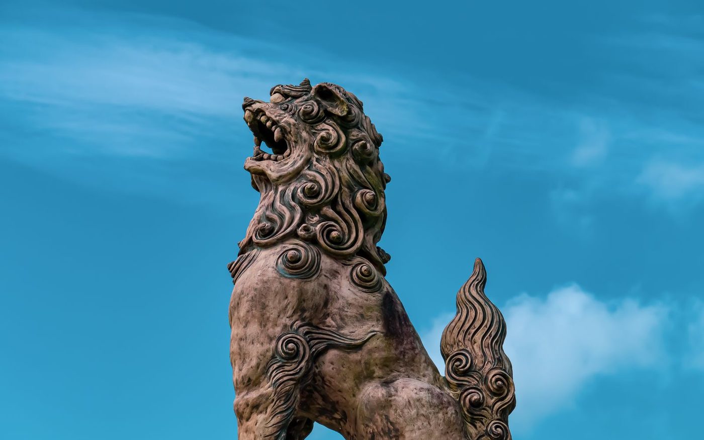 A large shisa lion-dog statue on a stone plinth against a blue sky in Okinawa