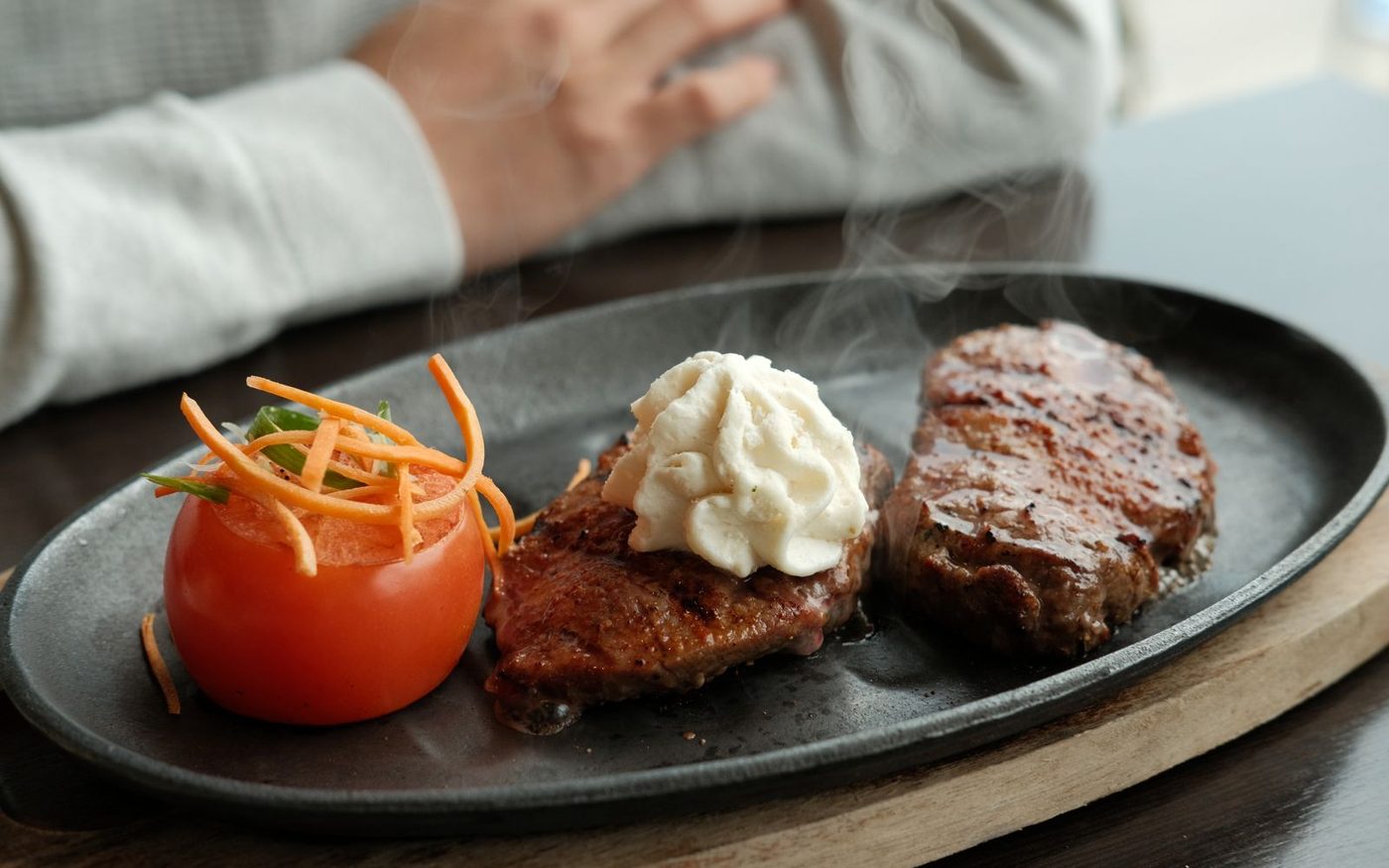 A steak on a plate with a tomato and a spoonful of butter