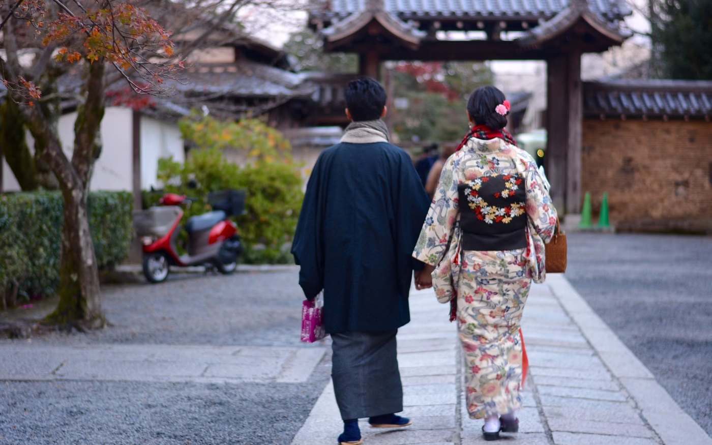 Two people in kimono walking a stone path between traditional buildings