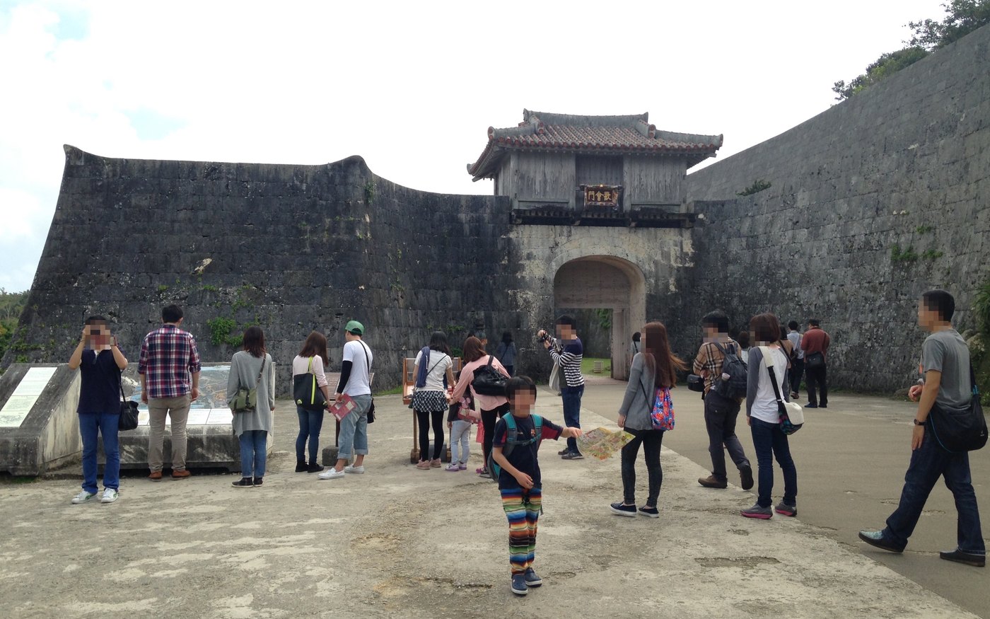 The stone wall and arched gate of Kankaimon at Shuri Castle, with a group of visitors in front of it