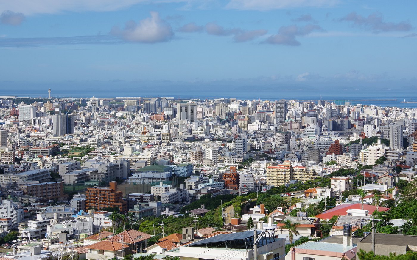 The city of Naha seen from Shuri Castle, red-tiled roofs in the foreground and the sea on the horizon