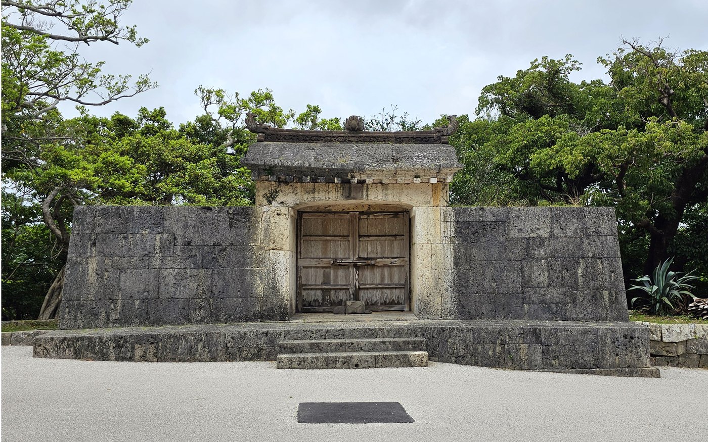 The weathered stone gate of Sonohyan-utaki with dark wooden doors, set among trees