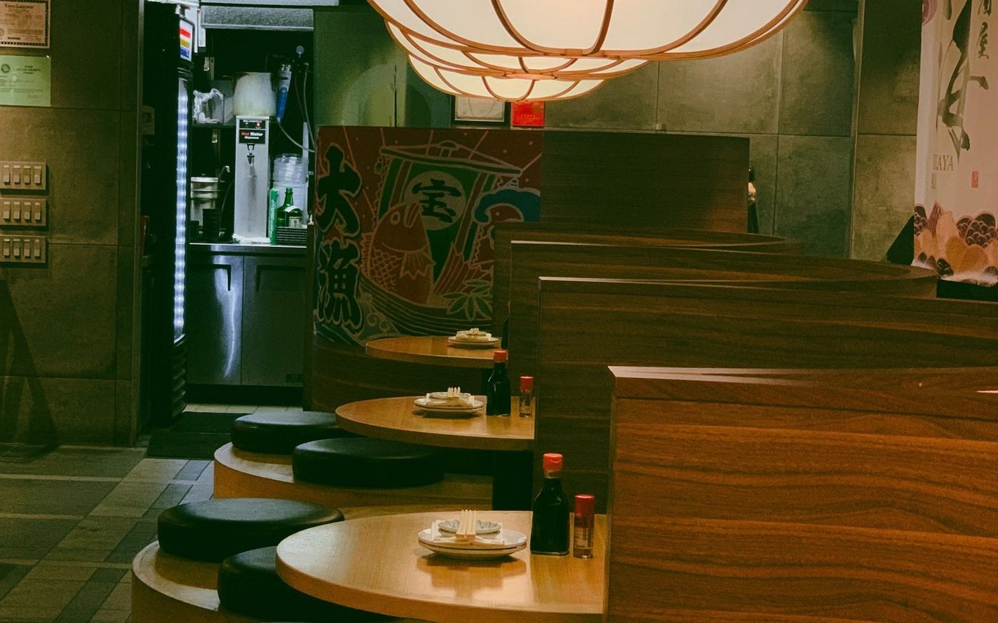 A row of booth tables in a Japanese restaurant, high wooden partitions between them, chopsticks and a soy sauce bottle on the table