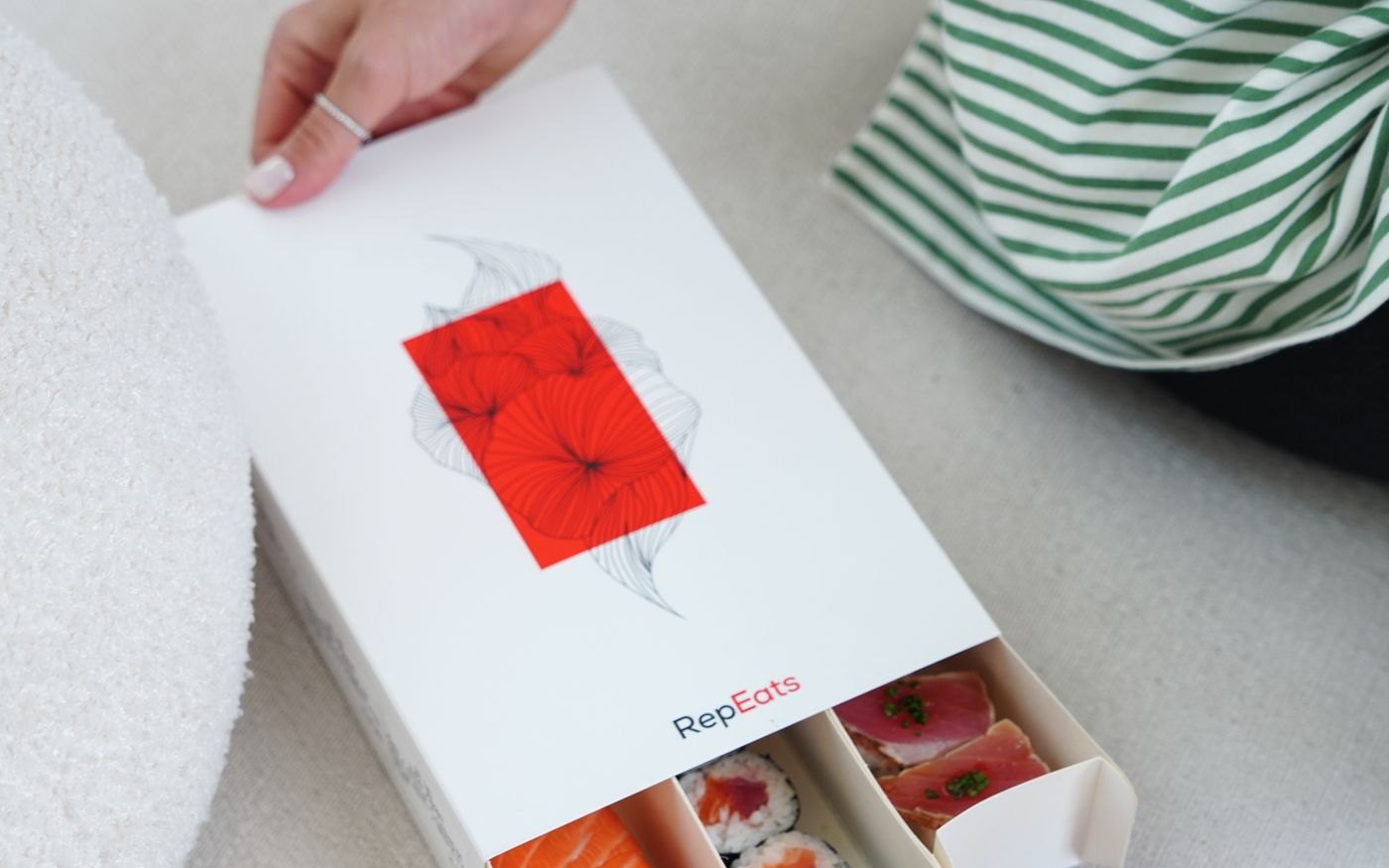 An open white takeaway box of sushi with salmon, rolls and seared fish, chopsticks resting across it