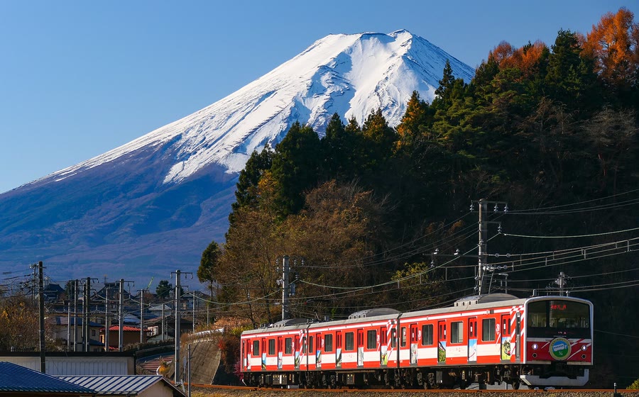 A red Fujikyu Railway train on the line with Mount Fuji behind it