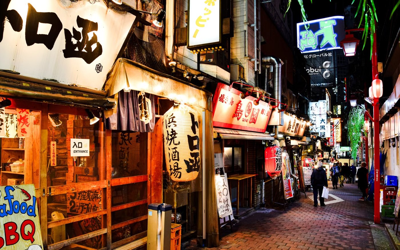 A narrow Shinjuku lane at night lined with small bars, their signs lit