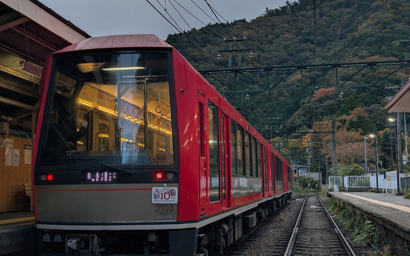 A red and cream Hakone Tozan Railway two-car train on a curve among trees