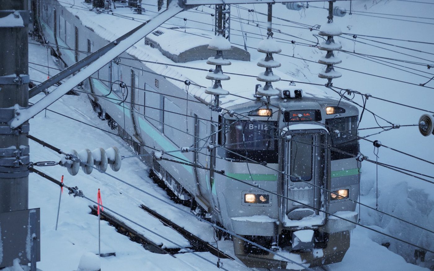 A train on a snow-covered railway track under overhead wires