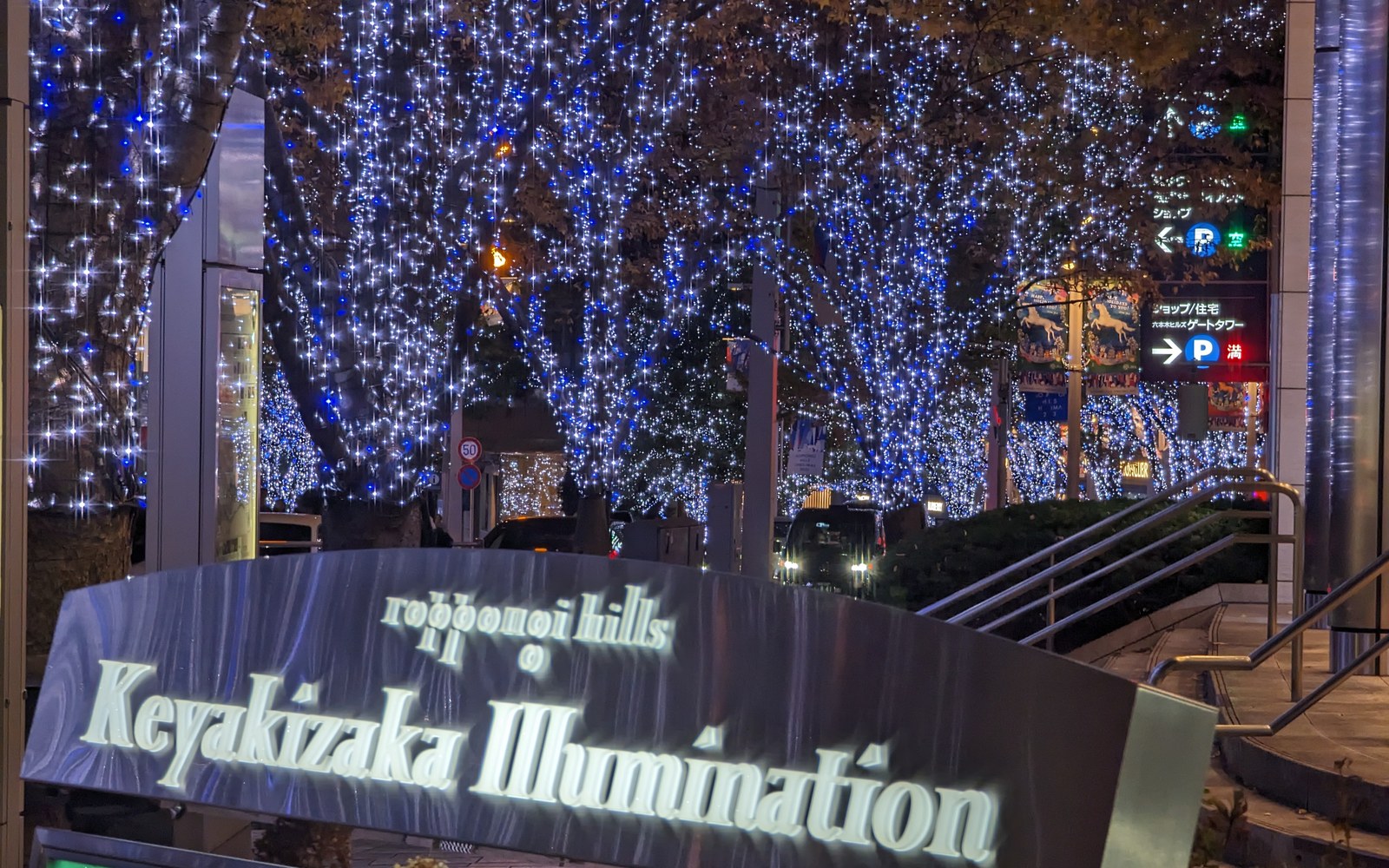 The Roppongi Hills Keyakizaka Illumination sign at night, with blue-lit trees behind