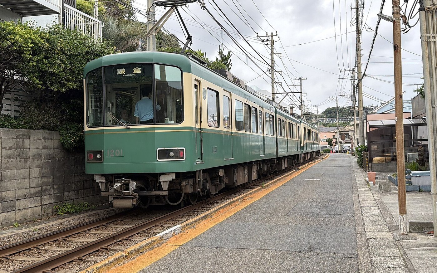 A cream and green Enoden tram running along the street on the Kamakura coast