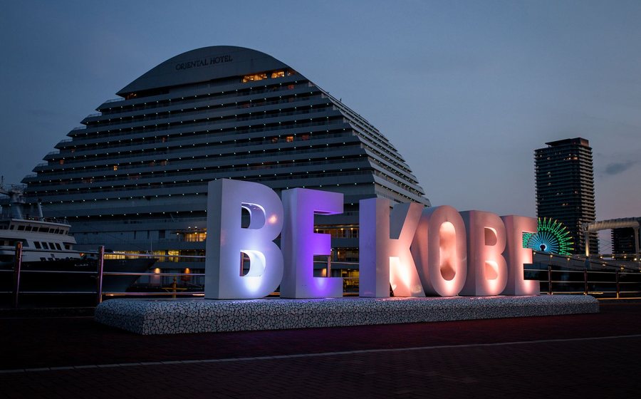 The BE KOBE sign at Meriken Park at dusk, with the Oriental Hotel behind it