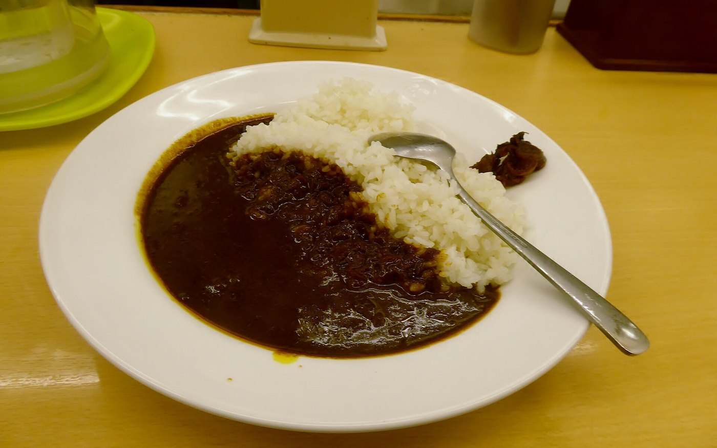 A plate of Matsuya beef curry and rice with a spoon, seen from above on a yellow-topped table