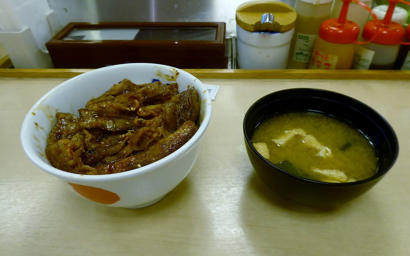 A Matsuya grilled beef bowl with green onion on top beside a bowl of soup