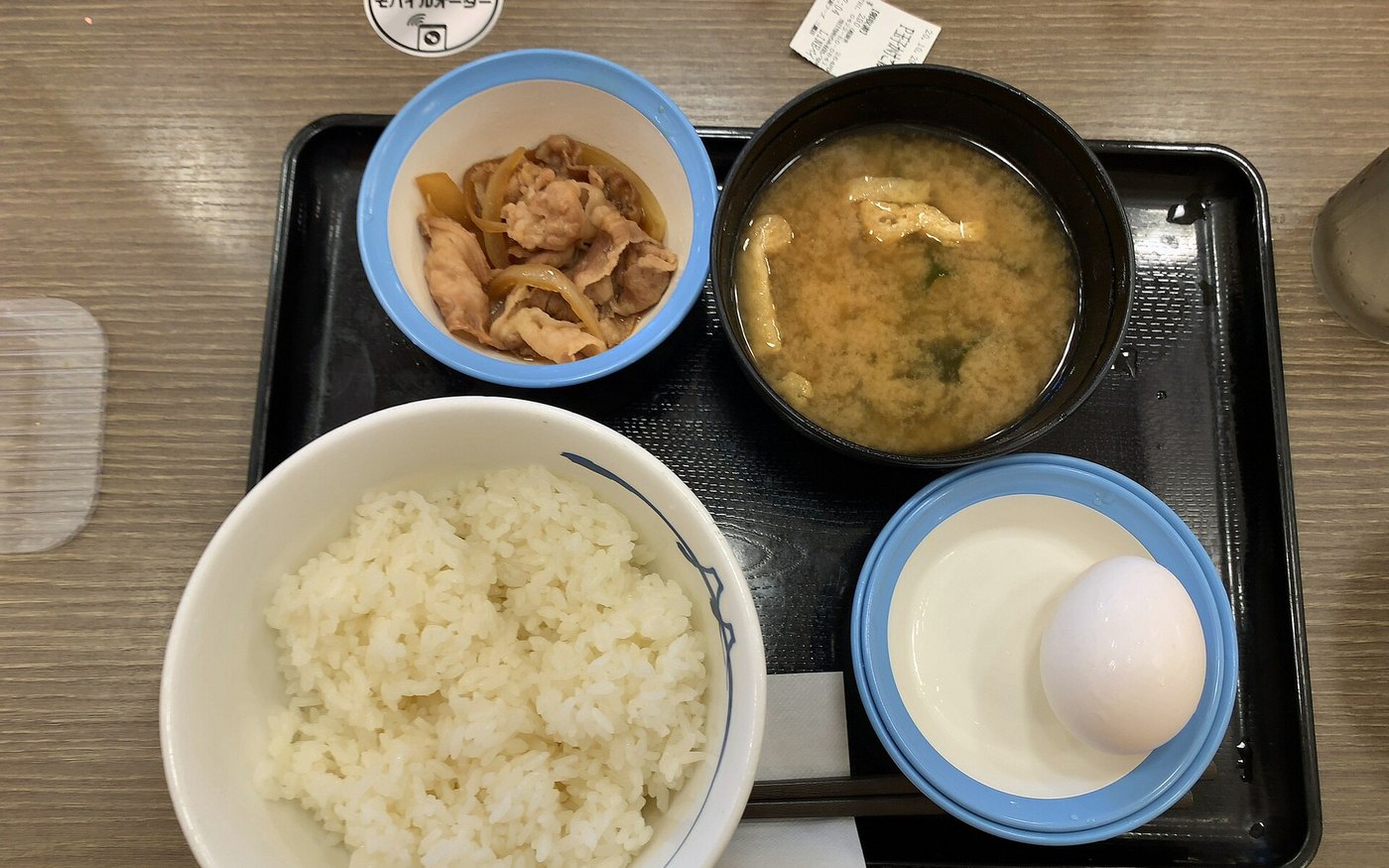 A Matsuya morning set on a tray: rice, miso soup, a small beef plate, pickles and a raw egg in a blue dish