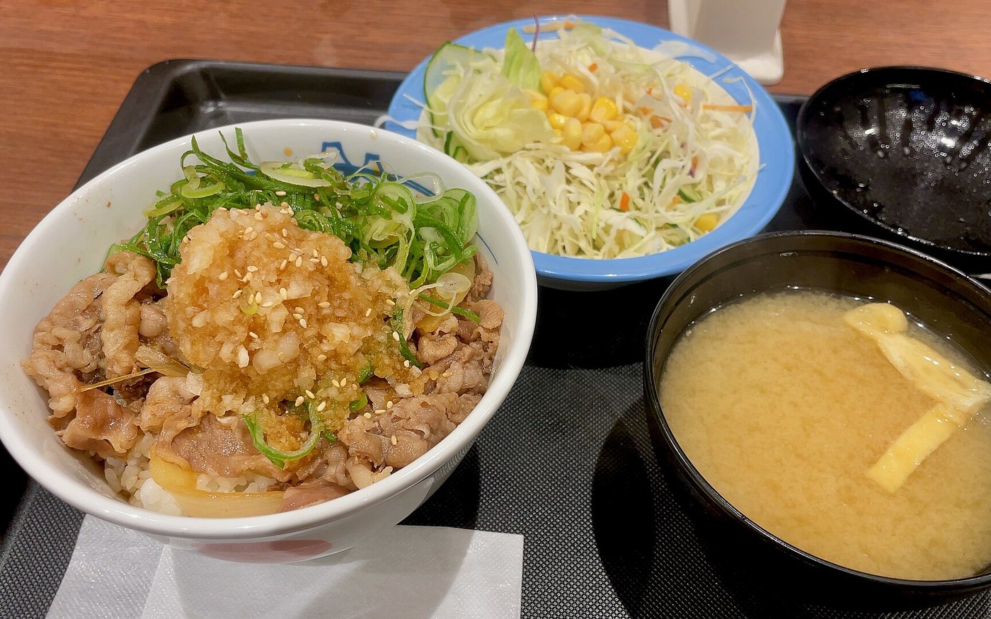 A Matsuya beef bowl topped with grated radish and ponzu on a tray with a salad, miso soup and pickles