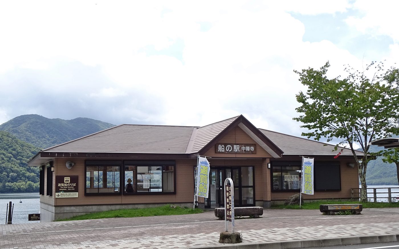 The low wooden building of the Chuzenji boat station beside the lake, with banners for the sightseeing boat