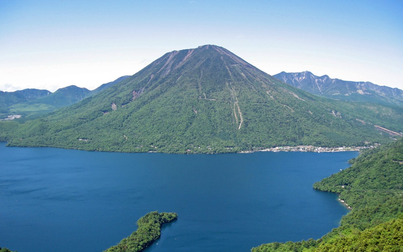 Lake Chuzenji seen from above, a forested mountain across the water and a village on the far shore