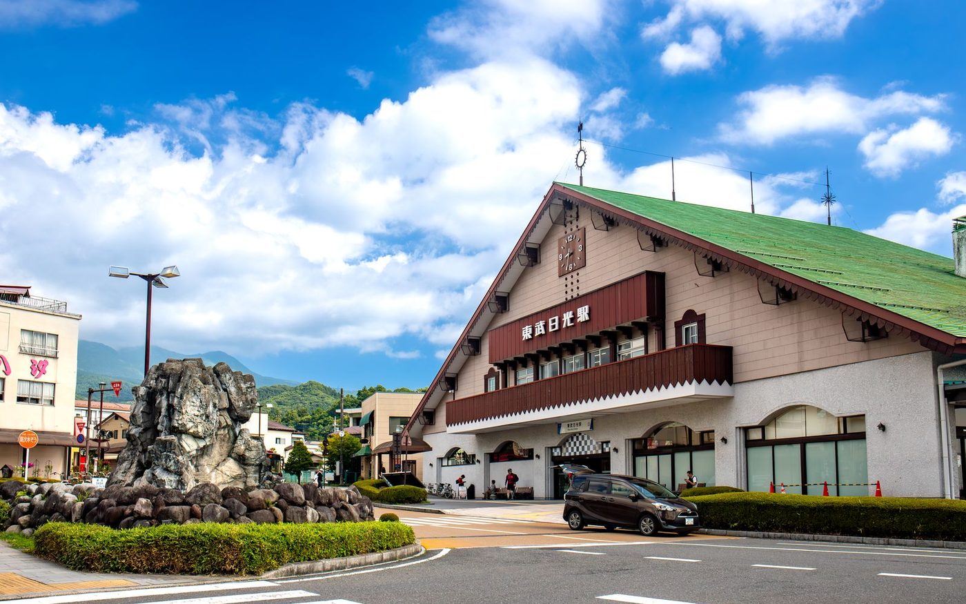 The green-roofed Tobu-Nikko station building with a clock on its gable and a bus turning in front of it