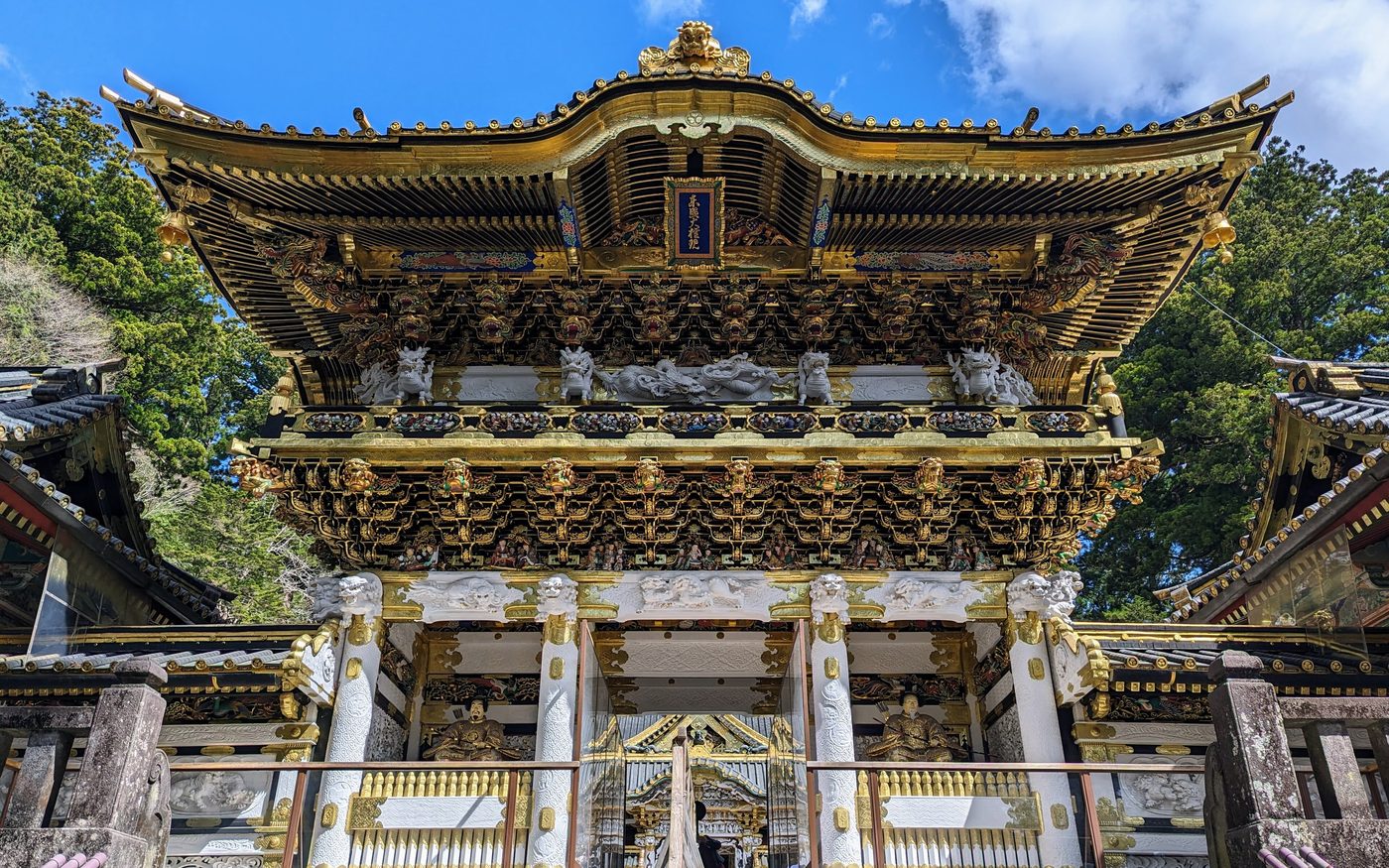 The gold and white carved facade of the Yomeimon gate at Nikko Toshogu under a blue sky