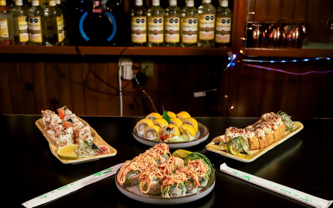 Platters of sushi rolls and sashimi on a dark restaurant table, with lemon and garnishes